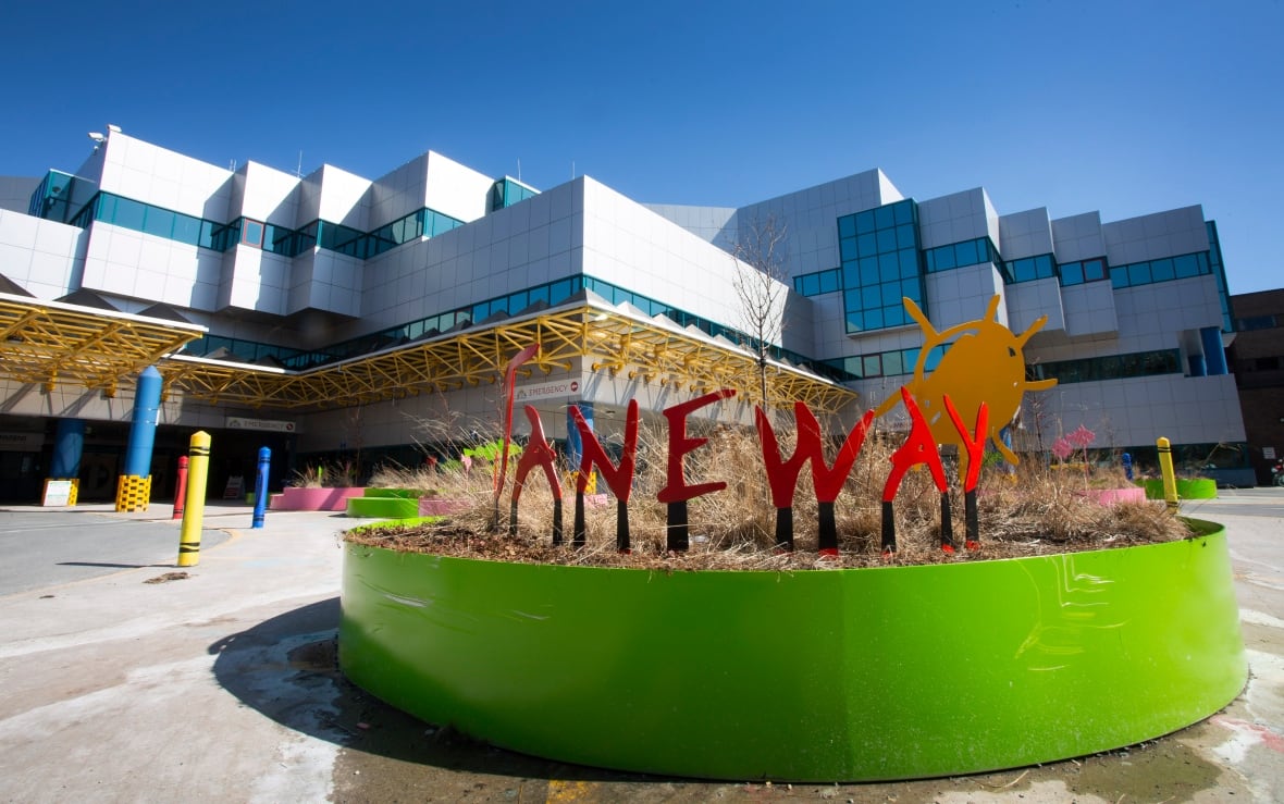 A green flower box flourishes in the sun outside a large, modern hospital building.