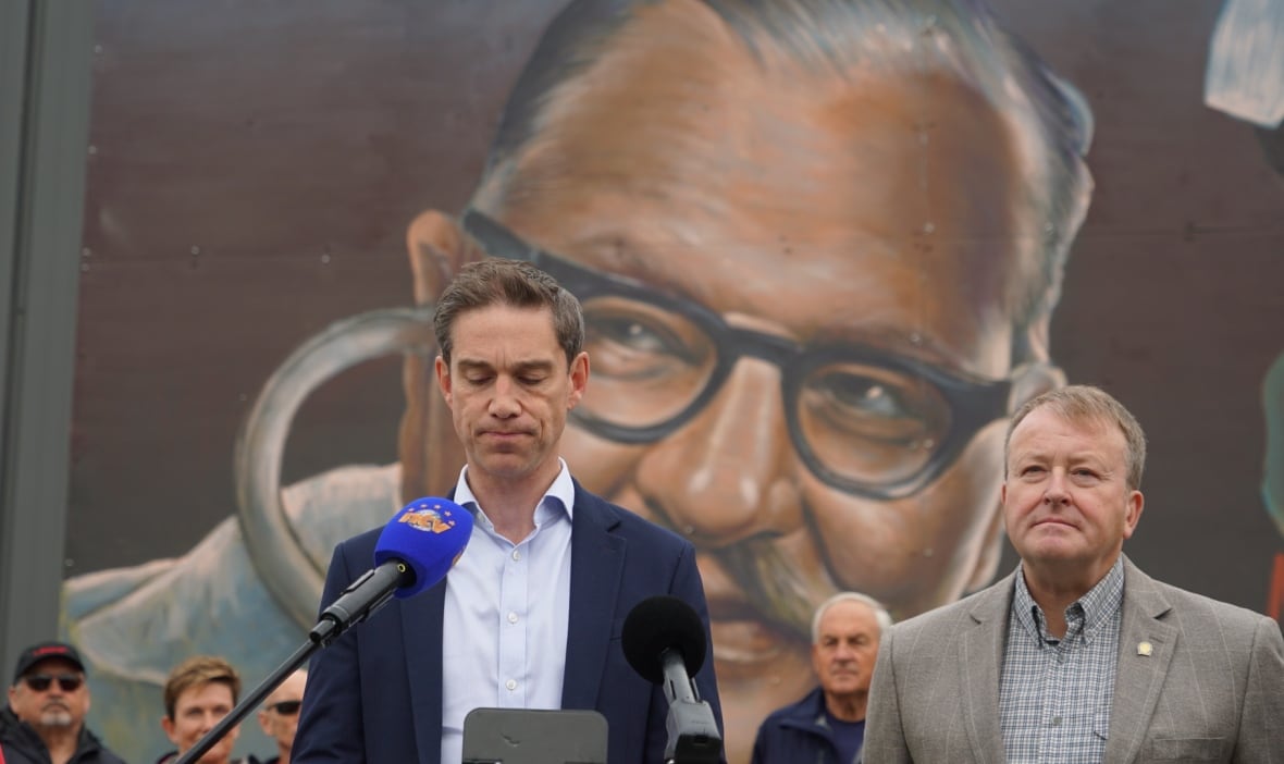 Two men stand in front of a mural of another man.