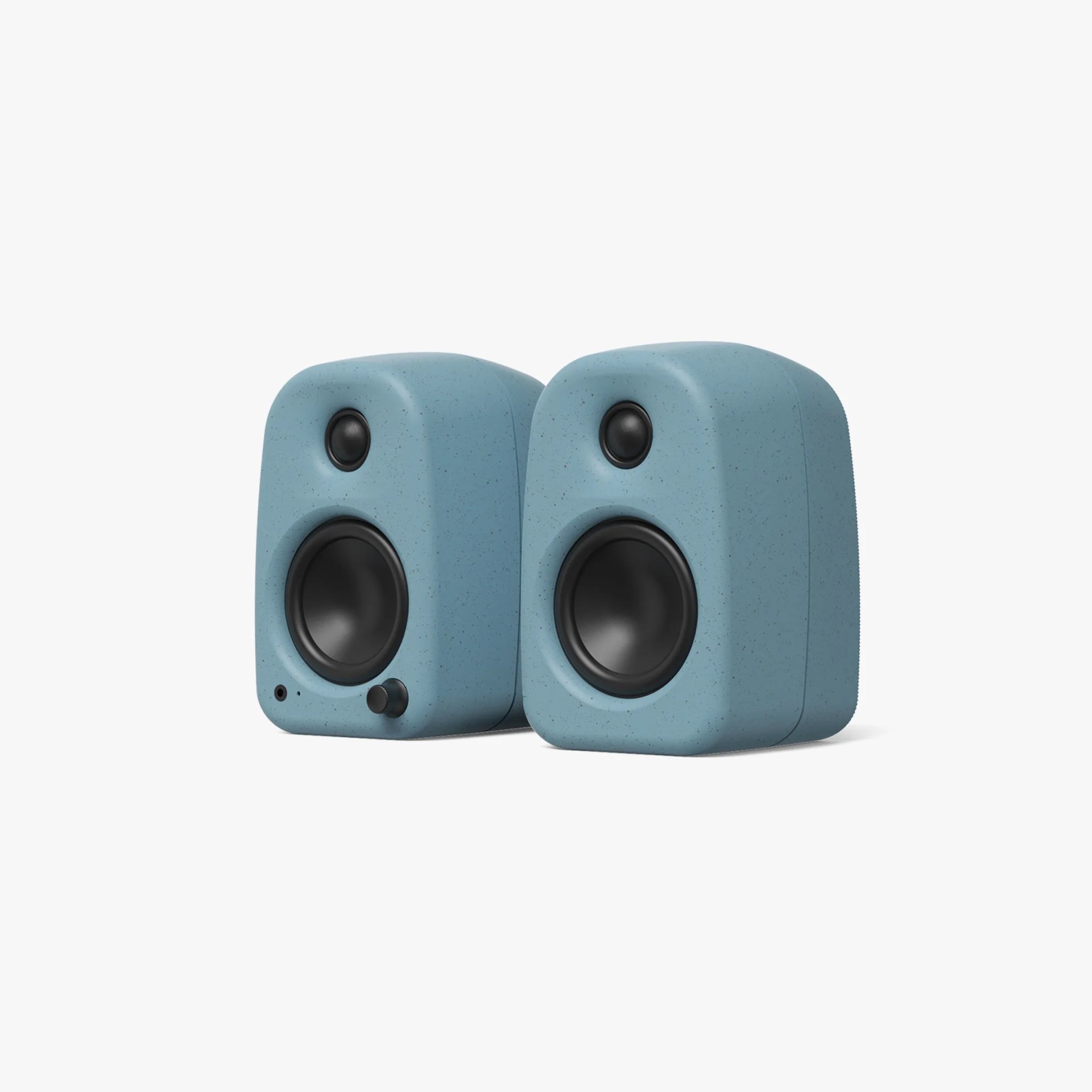 A pair of compact, rounded rectangular speakers in a speckled light blue color. Each speaker has a black circular woofer and a smaller black tweeter above it. The left speaker features a small black volume knob and a headphone jack on the front lower left side. The design is minimalist and modern.