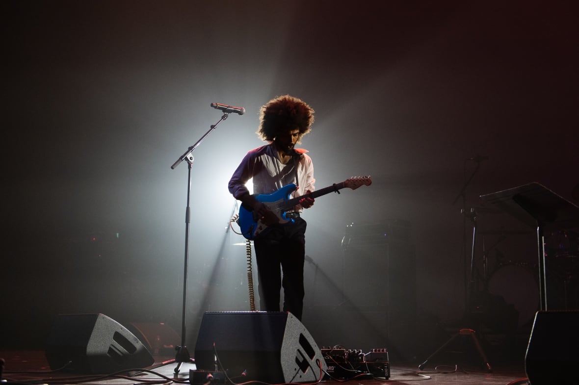 A Black musician playing solo guitar on the stage, illuminated by a spotlight on stage.
