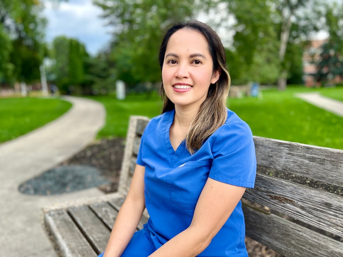 Woman in blue nurse scrubs sitting on bench in park.