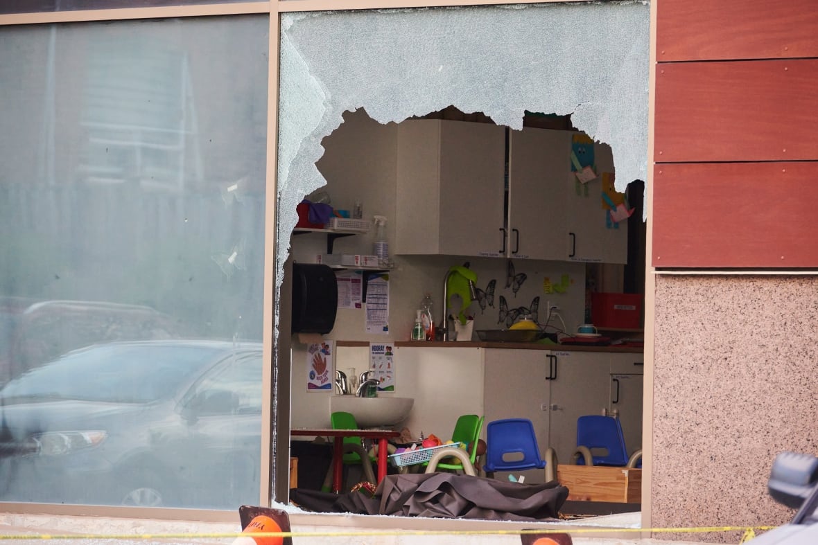 Behind a broken window are childrens' posters and chairs.