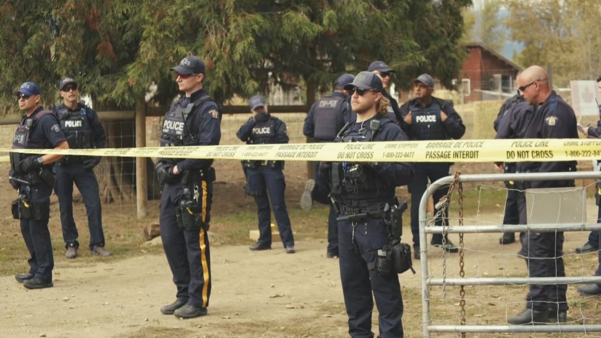 Nine police officers stand outside a farm gate, behind police tape.