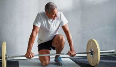Older man in activewear crouching next to a barbell in gym