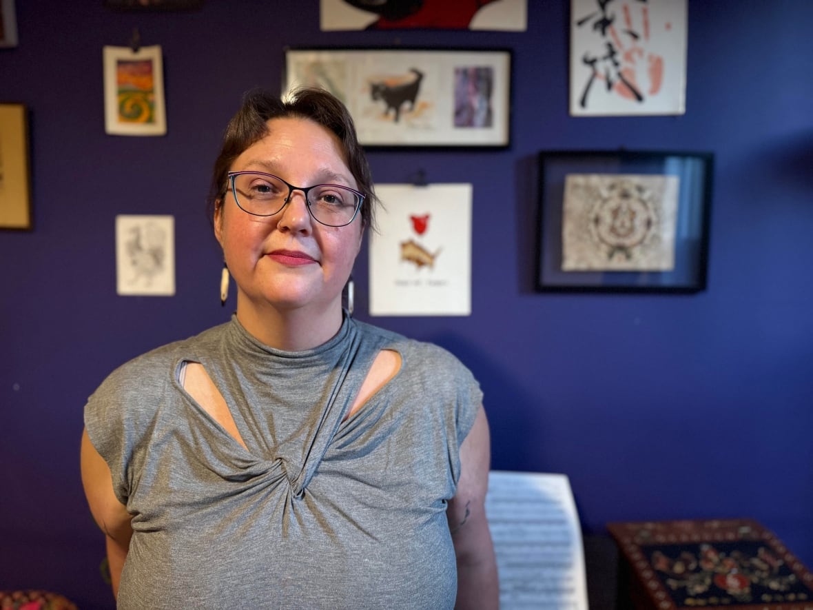 a woman standing against a wall with painting scattered behind her.