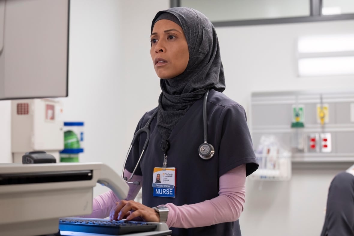 A woman in a hijab and hospital scrubs typing in front of a computer screen at a hospital.