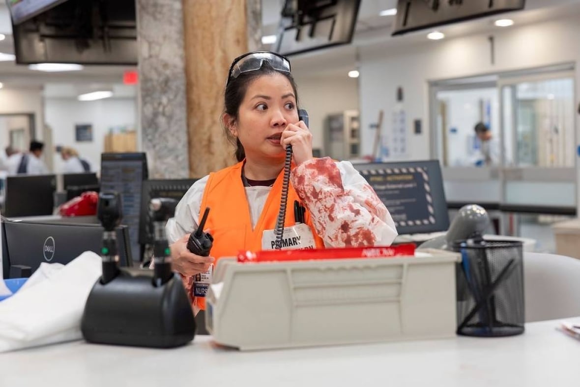 Nurse wearing bloody surgical gown and orange vest on the phone in the emergency room department.