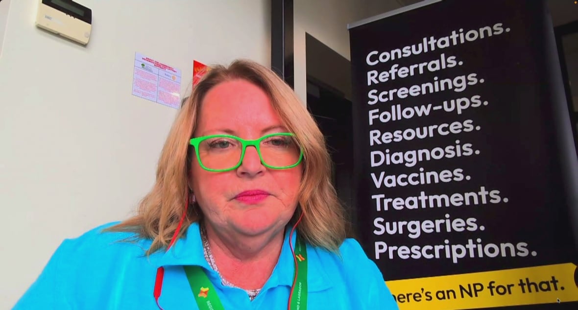 A woman wearing a blue shirt and bright green glasses sits in front of a banner in an office.