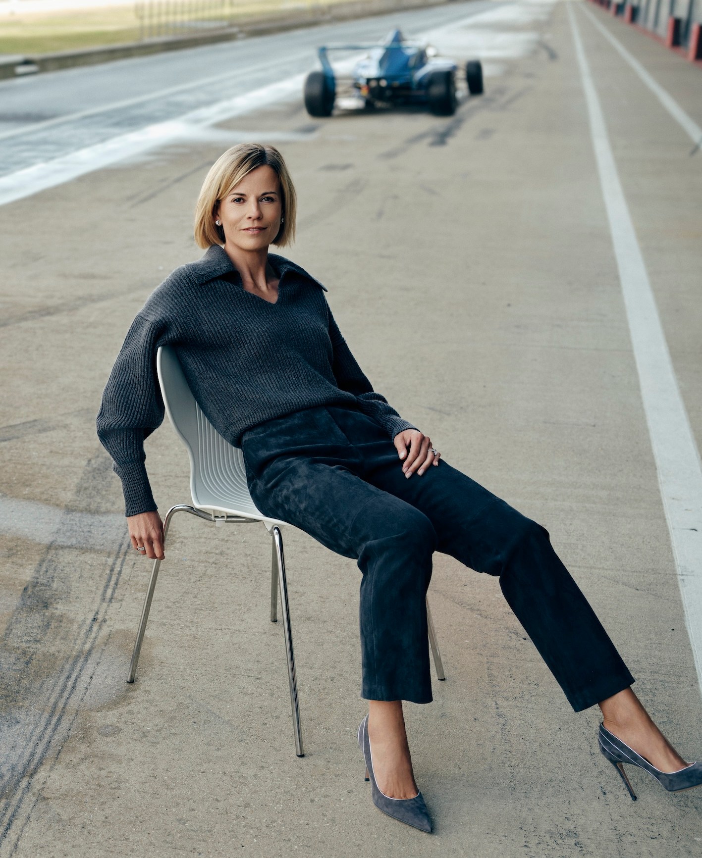 Susie Wolff, director of Venturi Racing, sits in a chair on a race track with a racing car in the background.
