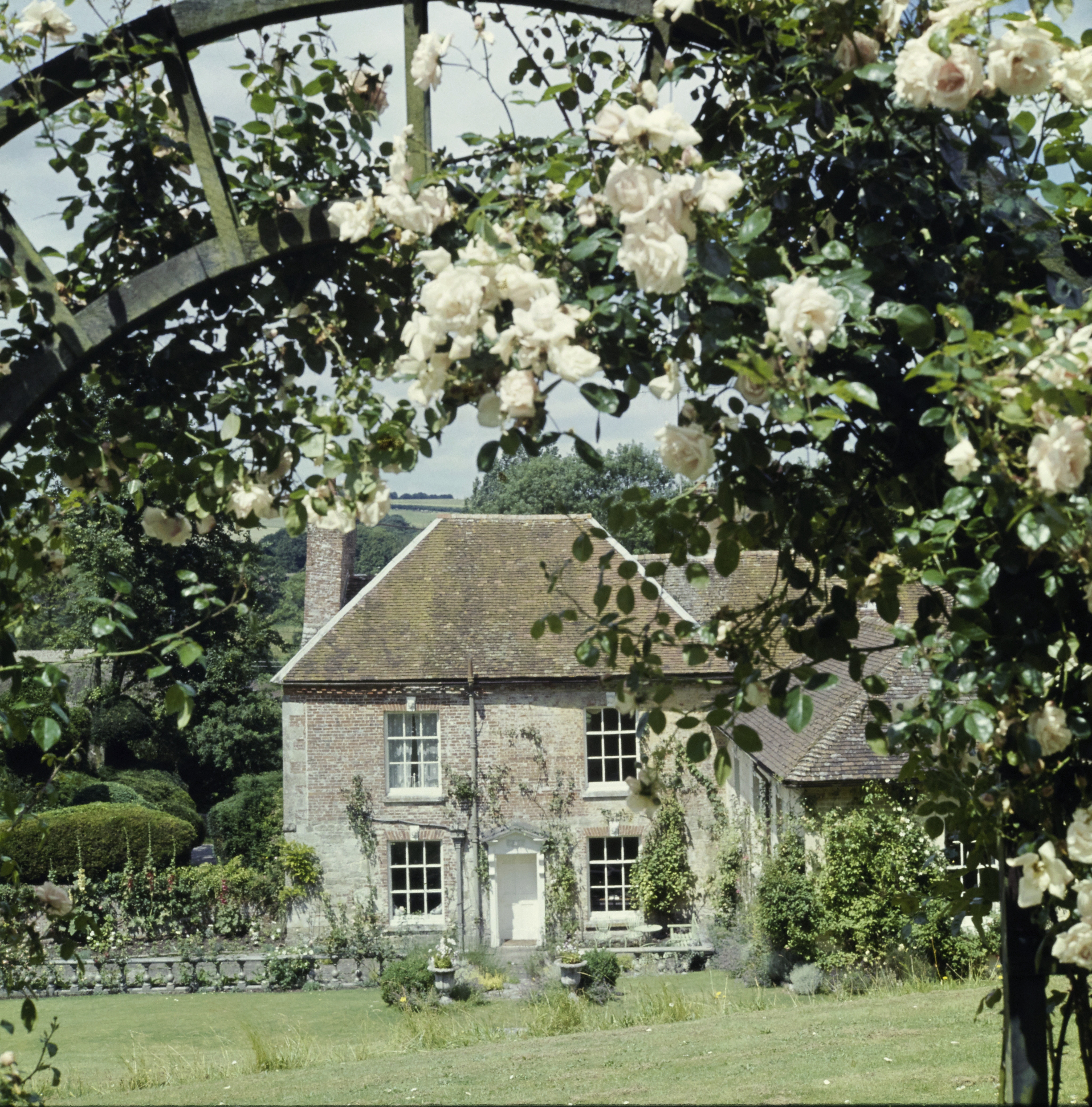 Exterior of Cecil Beaton's Reddish House in Wiltshire, England, seen through an arch of white climbing roses.