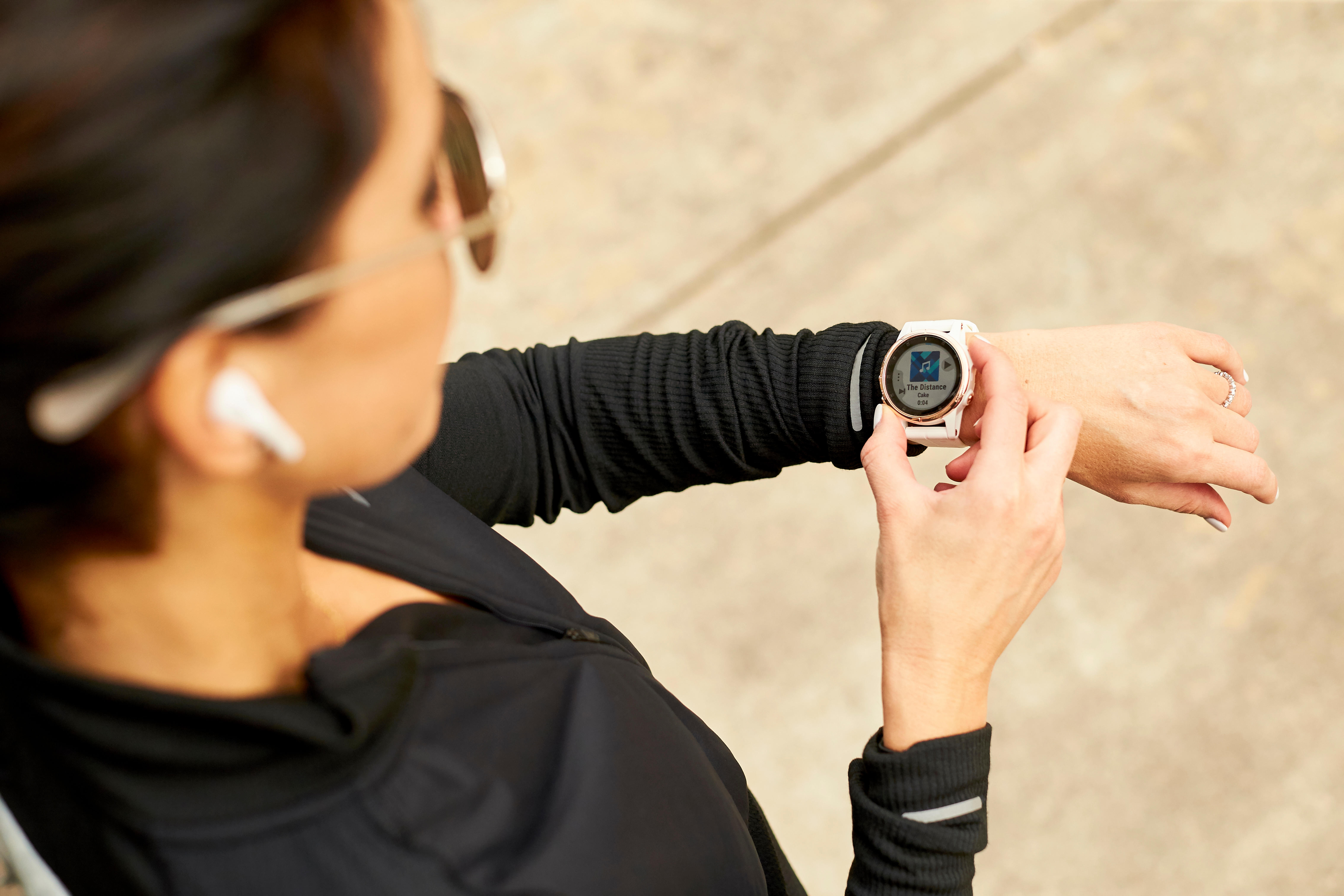 An overhead view of a woman wearing sunglasses and wireless earbuds, selecting music on her smartwatch.