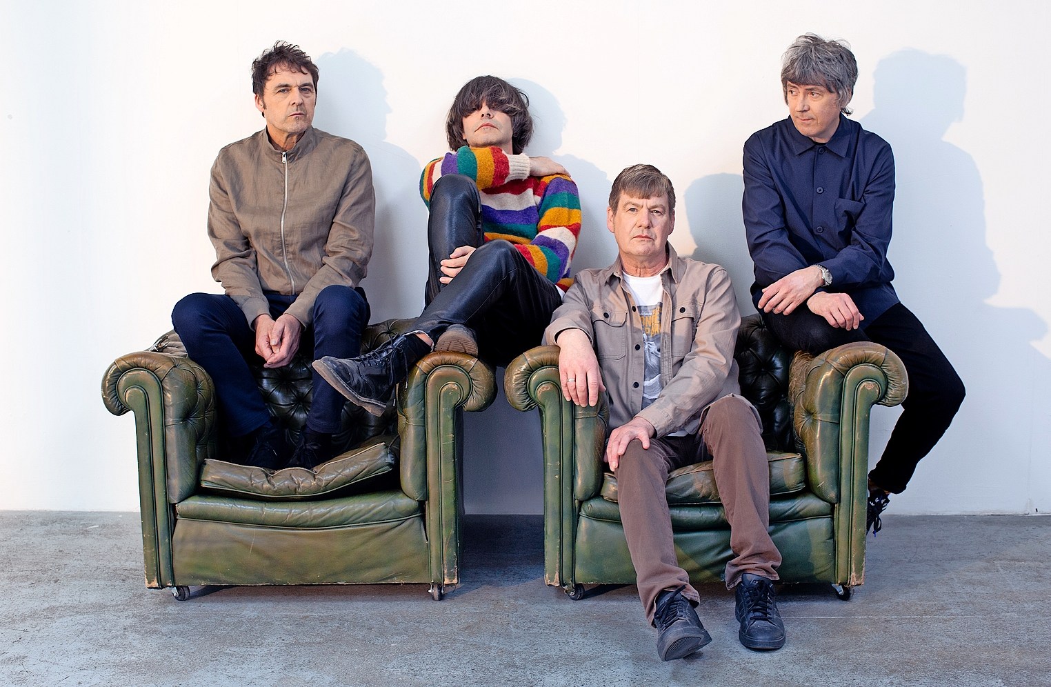 The Charlatans music group sitting on green leather chairs.