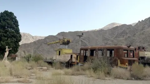 Rusted railway carriages and mountains on the backdrop