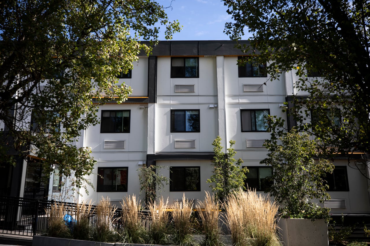 A three-storey apartment complex of repeated, windowed squares is framed by leafy trees.