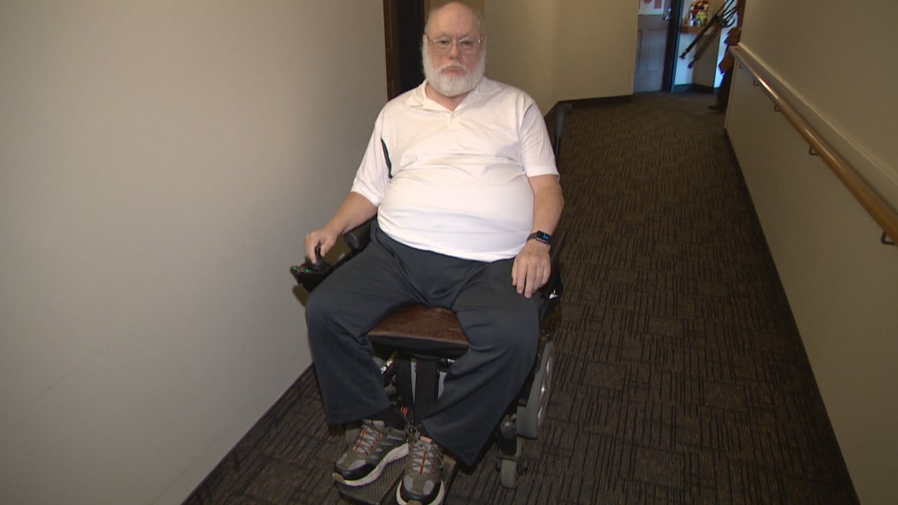 A man with a white shirt and bald head in a wheelchair 