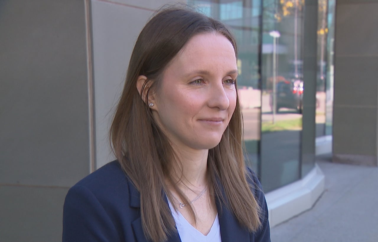 A woman with brown hair wearing a navy blue blazer looks off-camera