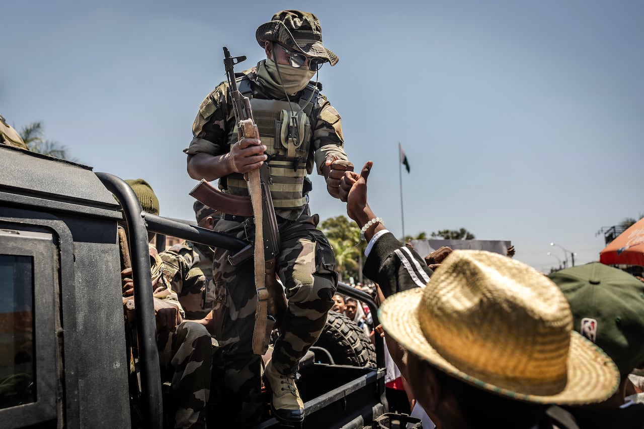 An armed soldier on the back of a pickup truck fist bumps a civilian on the road as a crowd gathers around.