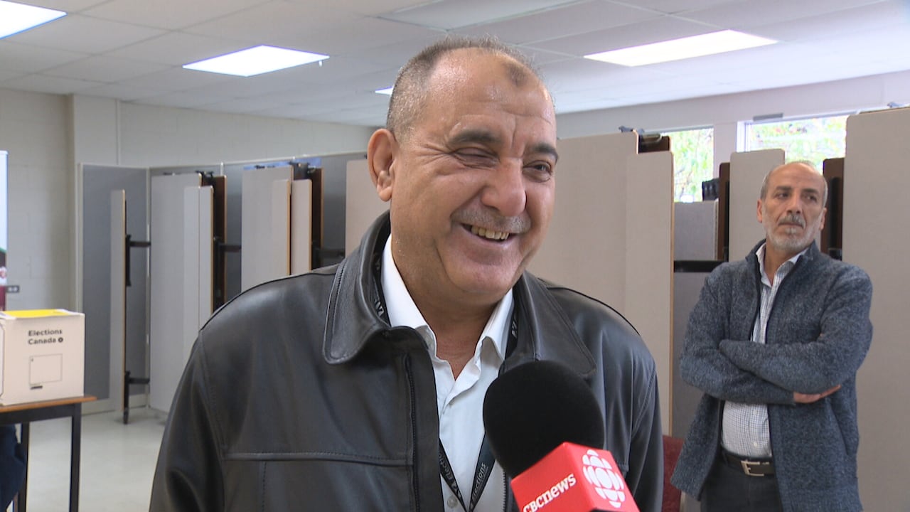 Middle-aged man smiling in classroom as he talks into mic held by reporter