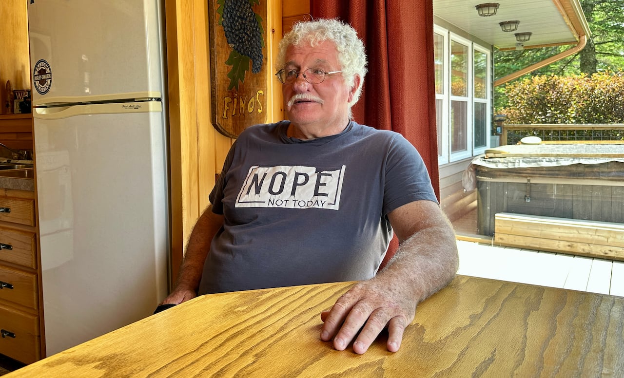 A man in a T-shirt sits at a kitchen table.