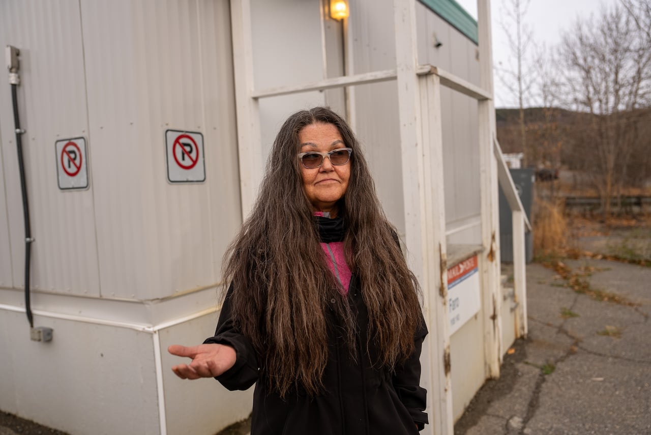 A woman stands outside of a small building.