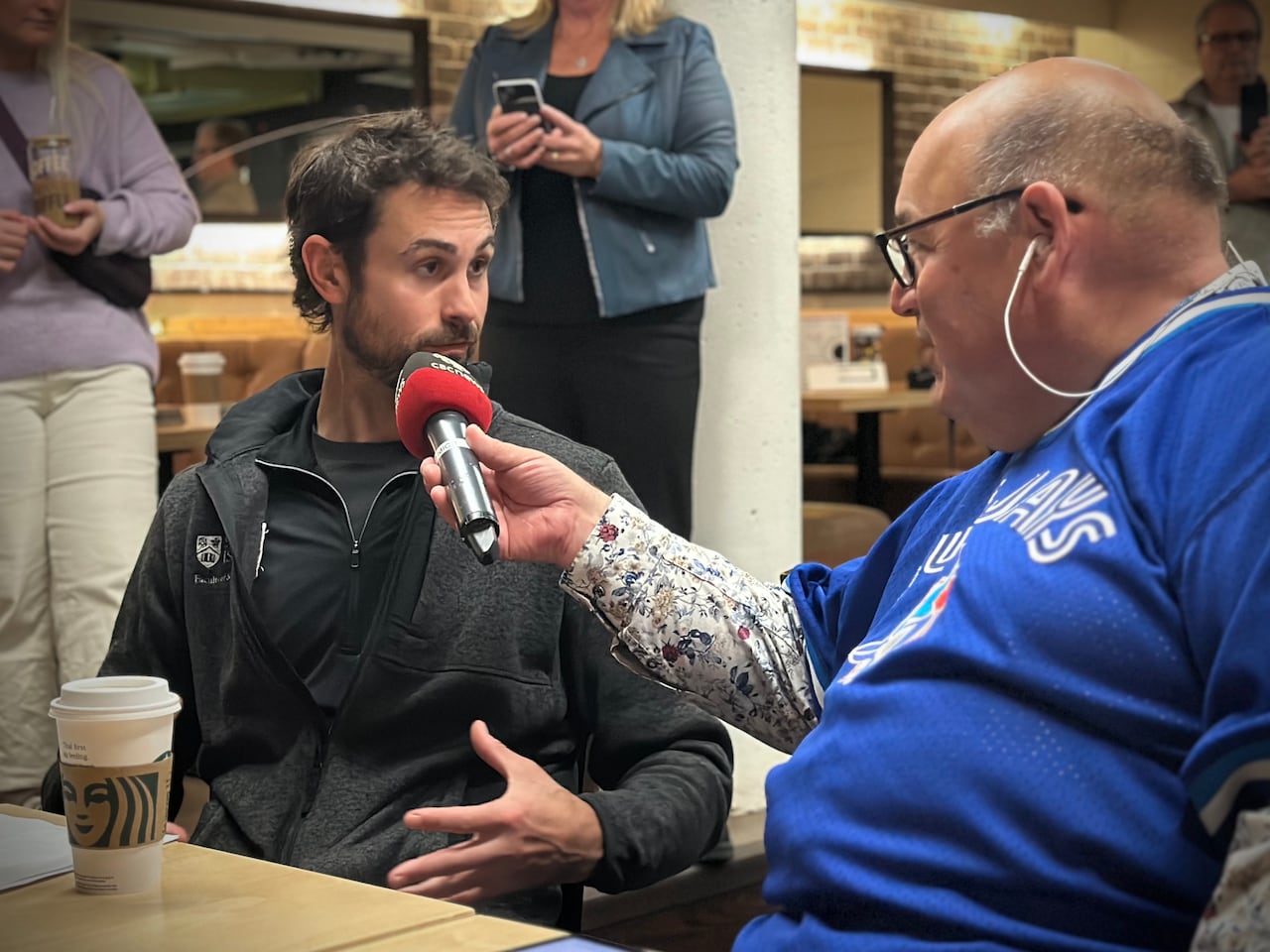A man being interviewed by a reporter holding a CBC News microphone