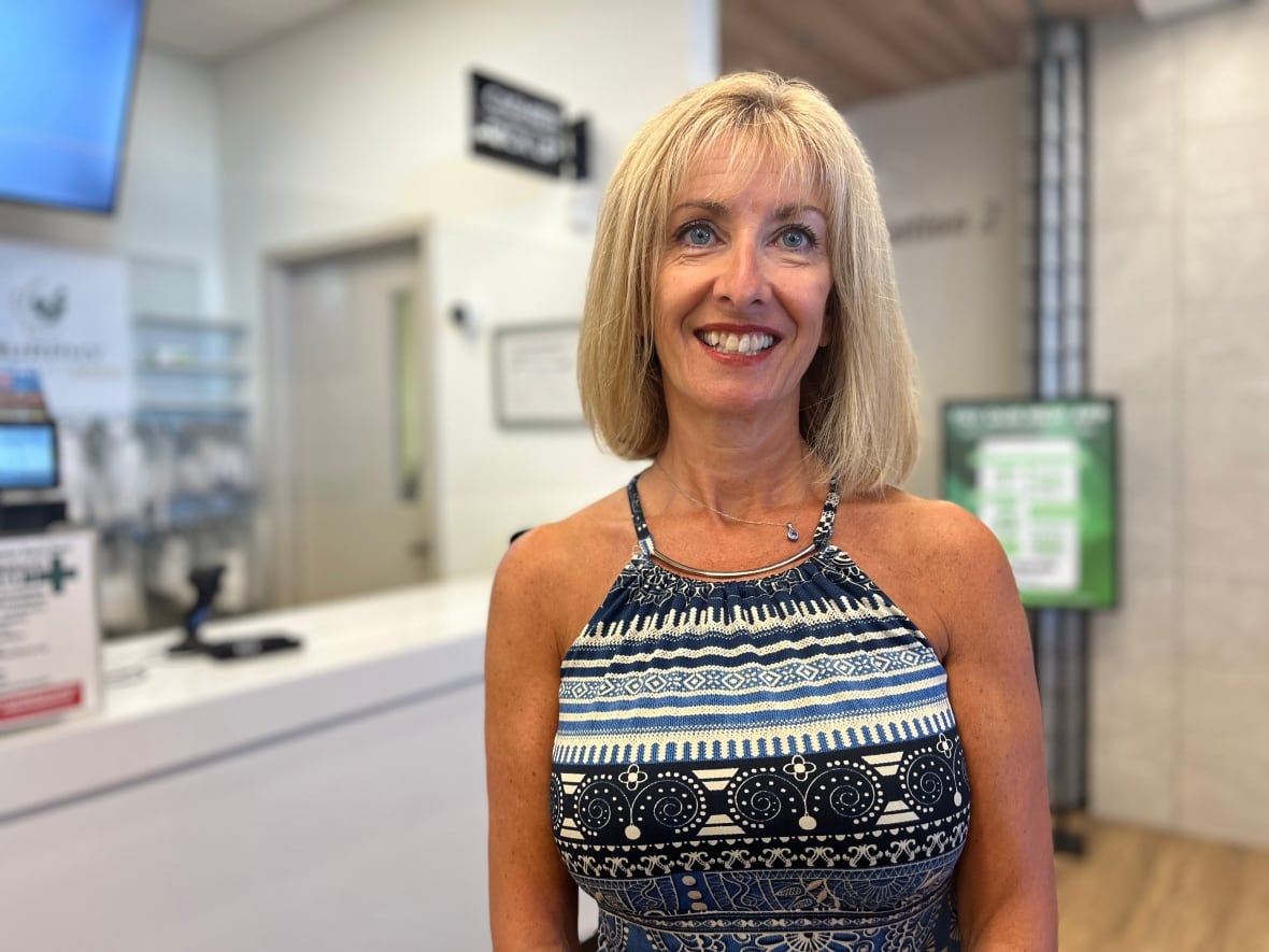 A woman stands in a pharmacy. She is smiling at the camera. 