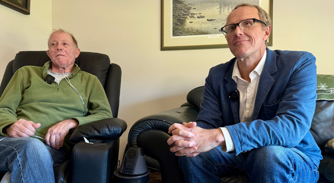 A man in a green sweater sits next to a man in a blue blazer.