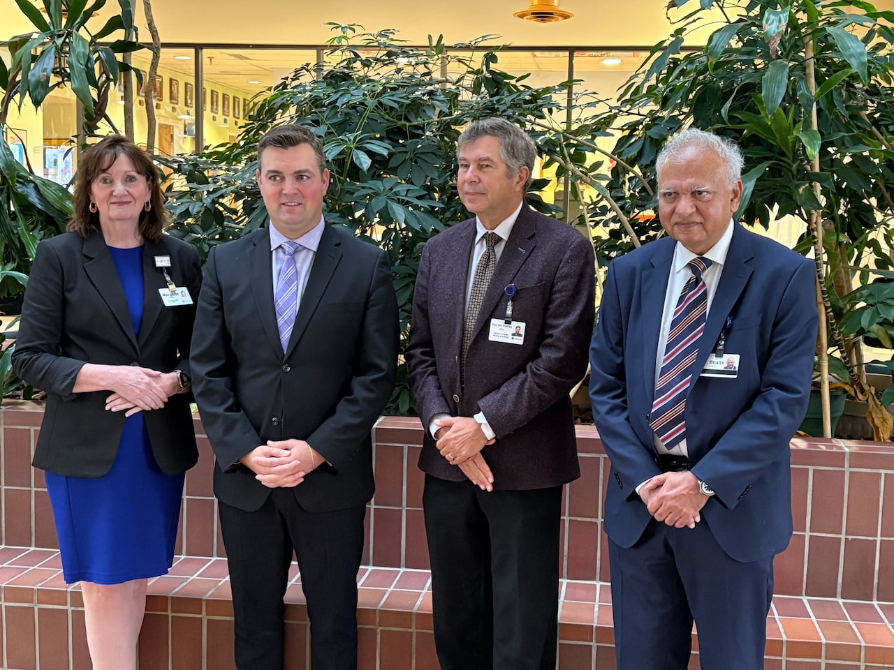 Three men and one woman standing side by side in a group photo all dressed in formal, business attire.