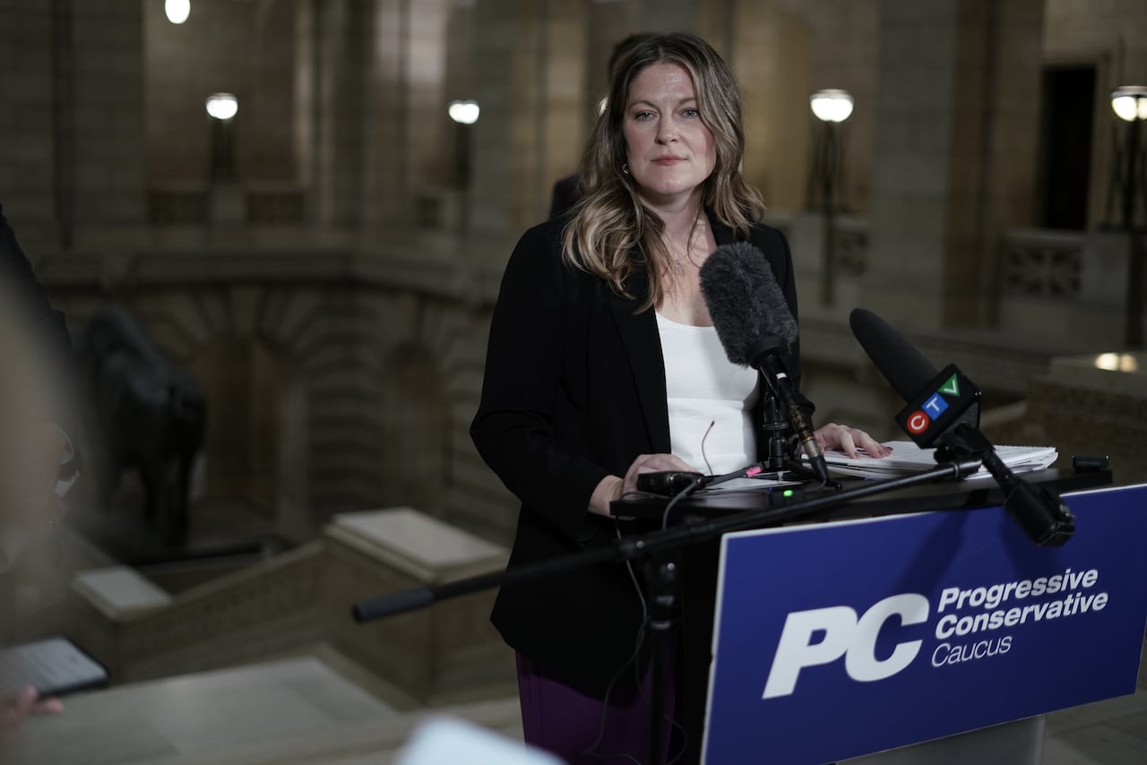 A woman in front of a podium with the logo of the Progressive Conservative party. It says 'Progressive Conservative Caucus'