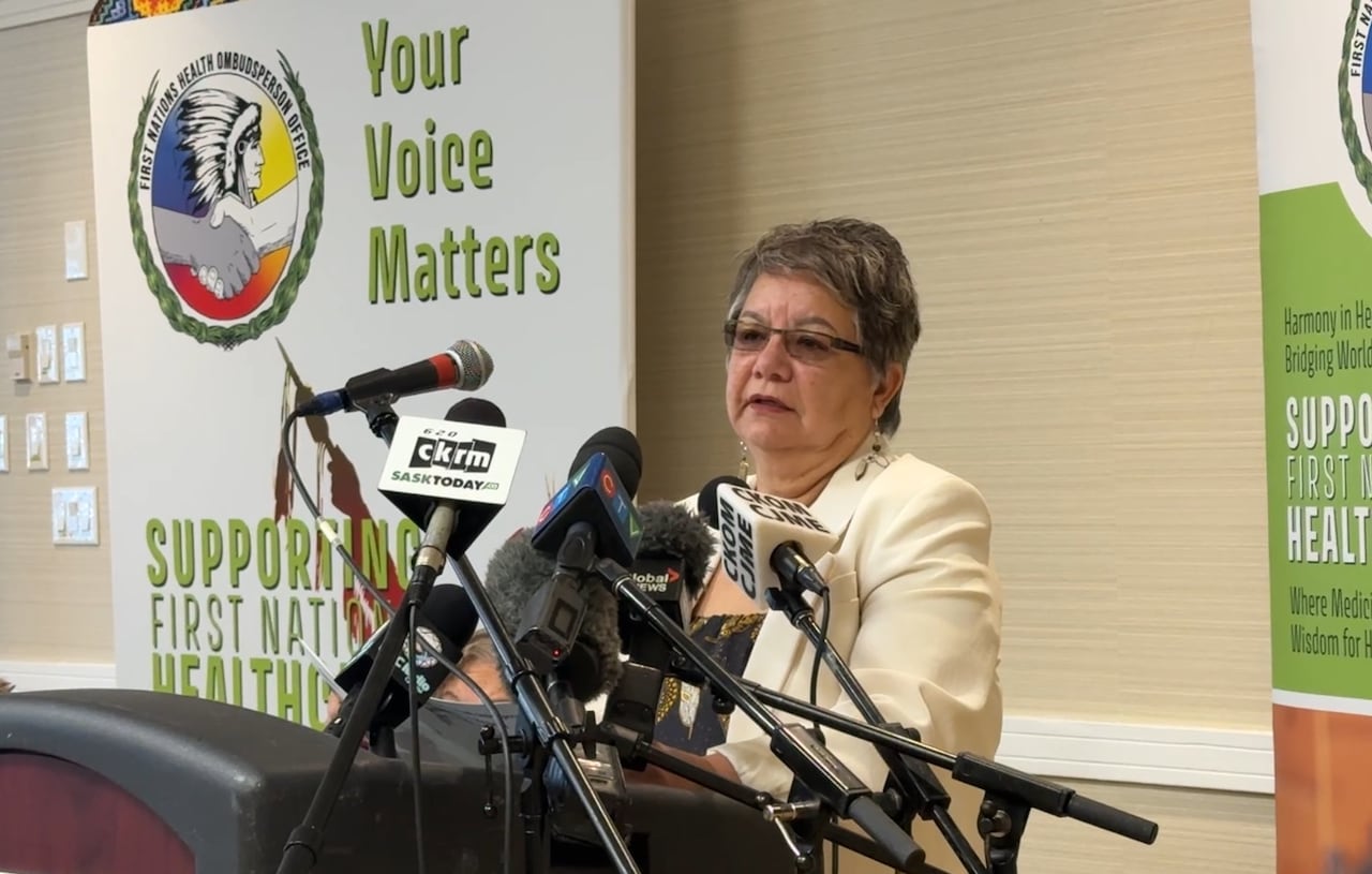 A woman in a white blazer stands at a podium with signs behind her.