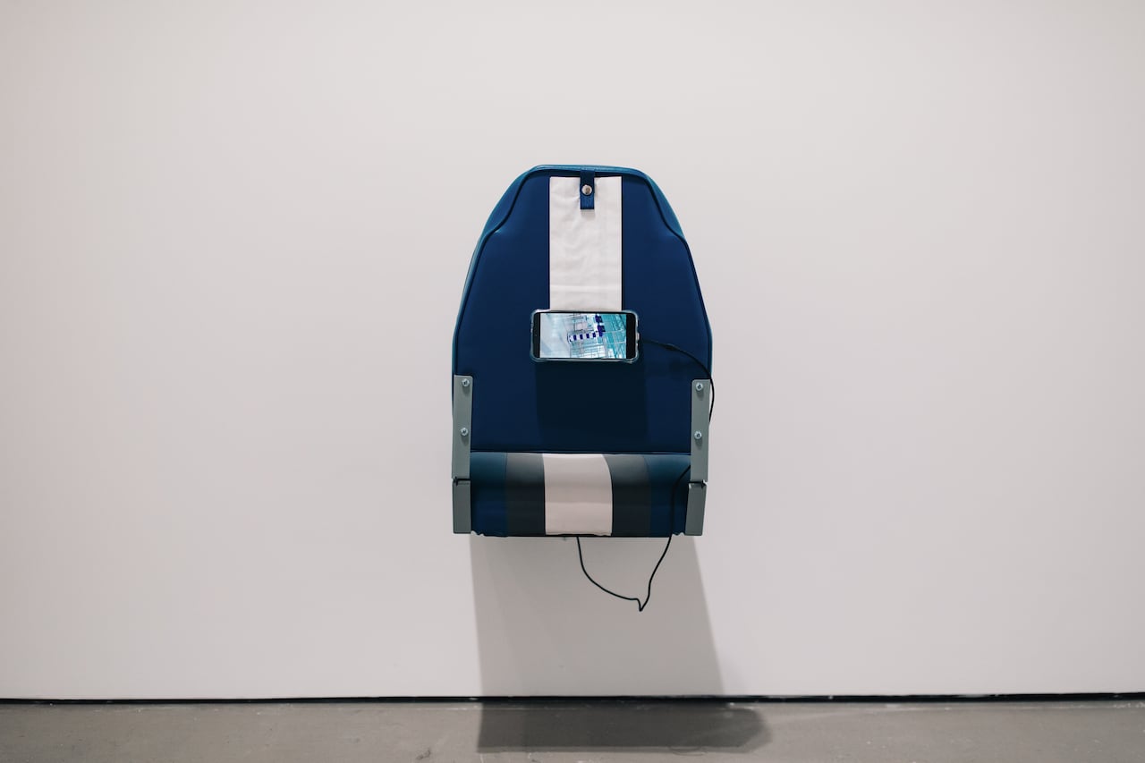 A boat seat with a cell phone displaying a video on it. 