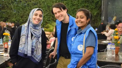 Refugee Crisis Foundation Mr Lugo (middle) stood with two other people - wearing blue jackets and smiling into the camera. 