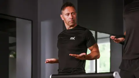 Handout Matt Kendrick trains another man at MK Health Hub. They are both wearing black. They are holding their hands out as they do a fitness exercise.