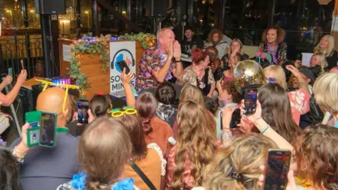 28thStreetMedia A large crowd of people gather around Norman Cook as he performs at an event.