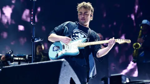 BBC Sam Fender performing on stage, holding a baby blue electric guitar. 