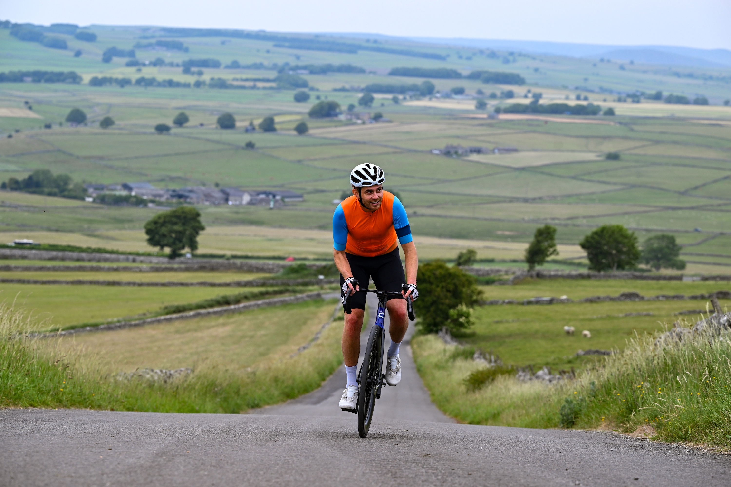 A male cyclist rides up a climb in an orange top