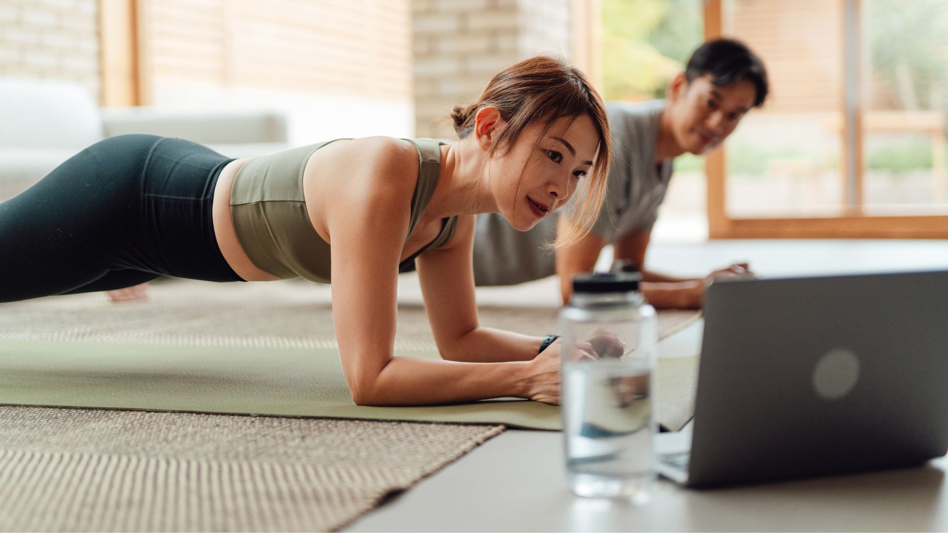 Woman doing plank exercise on yoga mat with laptop propped open