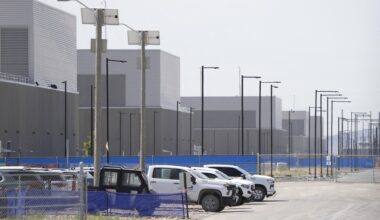 A wide shot of a rows of towering industrial-style buildings on the Utah desert. There are white pickup trucks parked in the foreground.