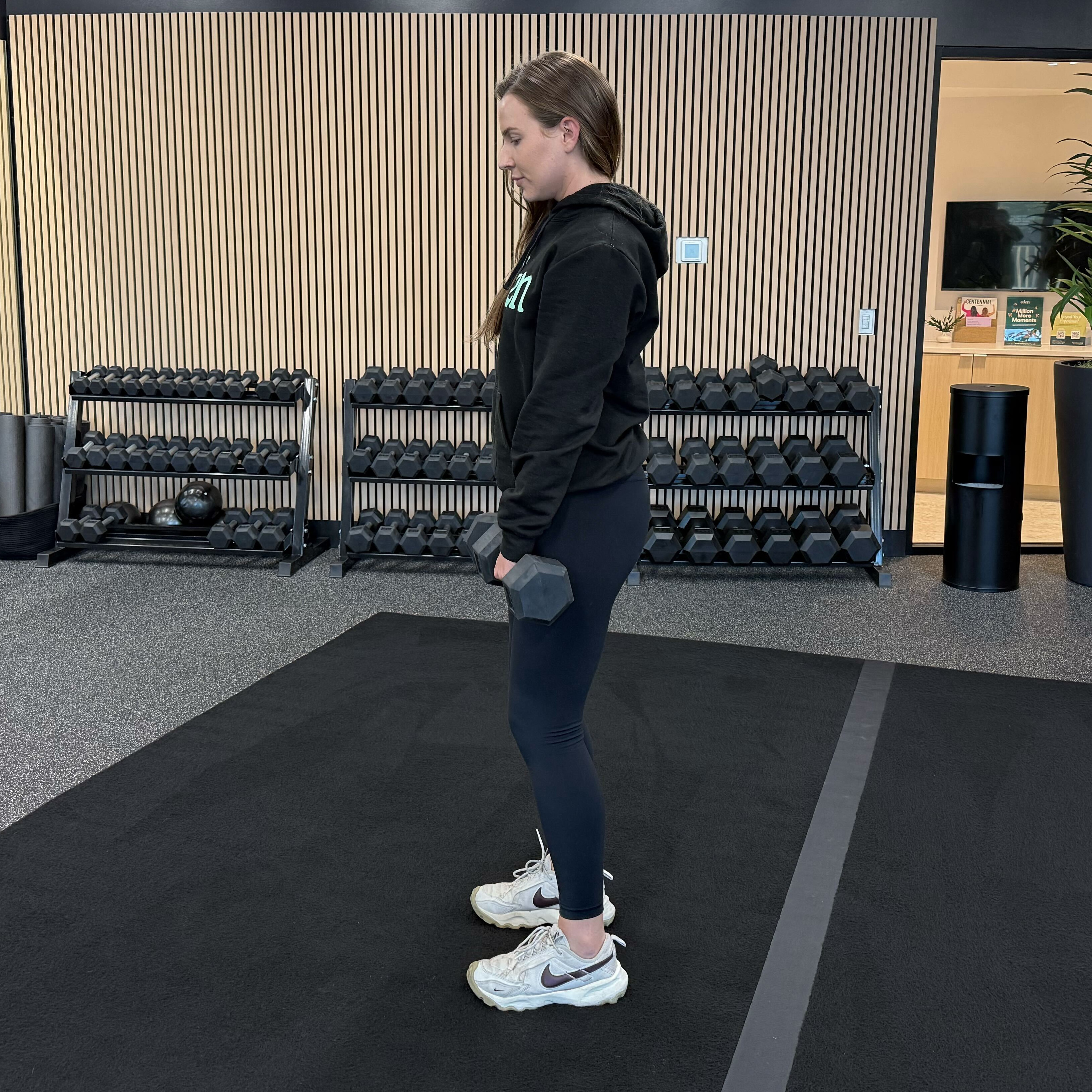 Felicia Hernandez, a personal trainer for Eden Health Club, performs a Romanian deadlift with dumbbells. She is standing with feet shoulder-width apart, dumbbells held at her hips.
