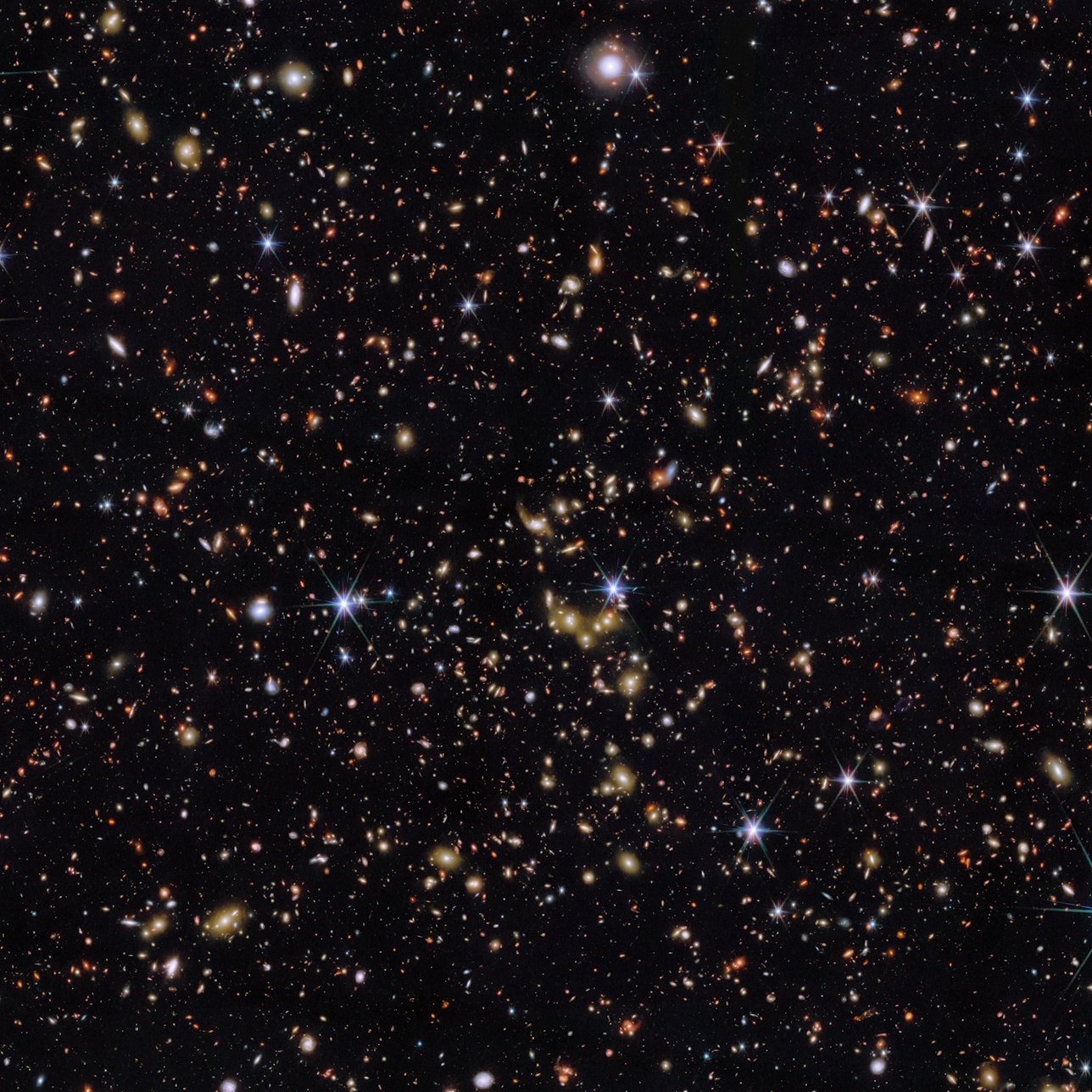 A dense field of stars and distant galaxies scattered across the dark backdrop of space, with some objects appearing as bright points and others as faint, diffuse shapes.