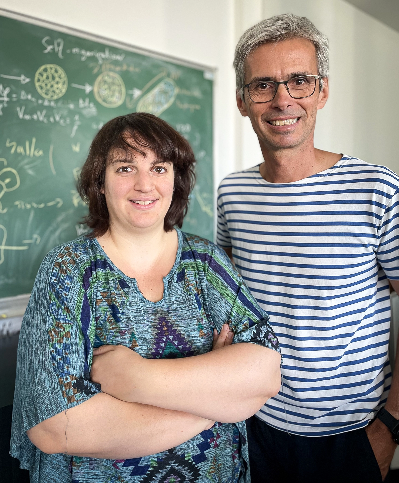 Two smiling researchers standing side by side in front of a blackboard.
