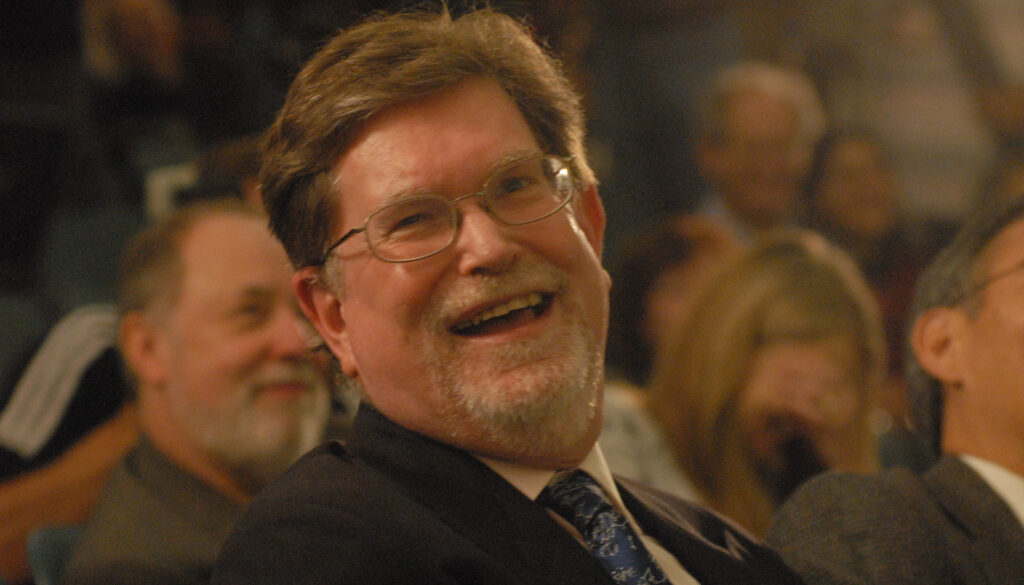 a smiling bearded man sitting in an auditorium