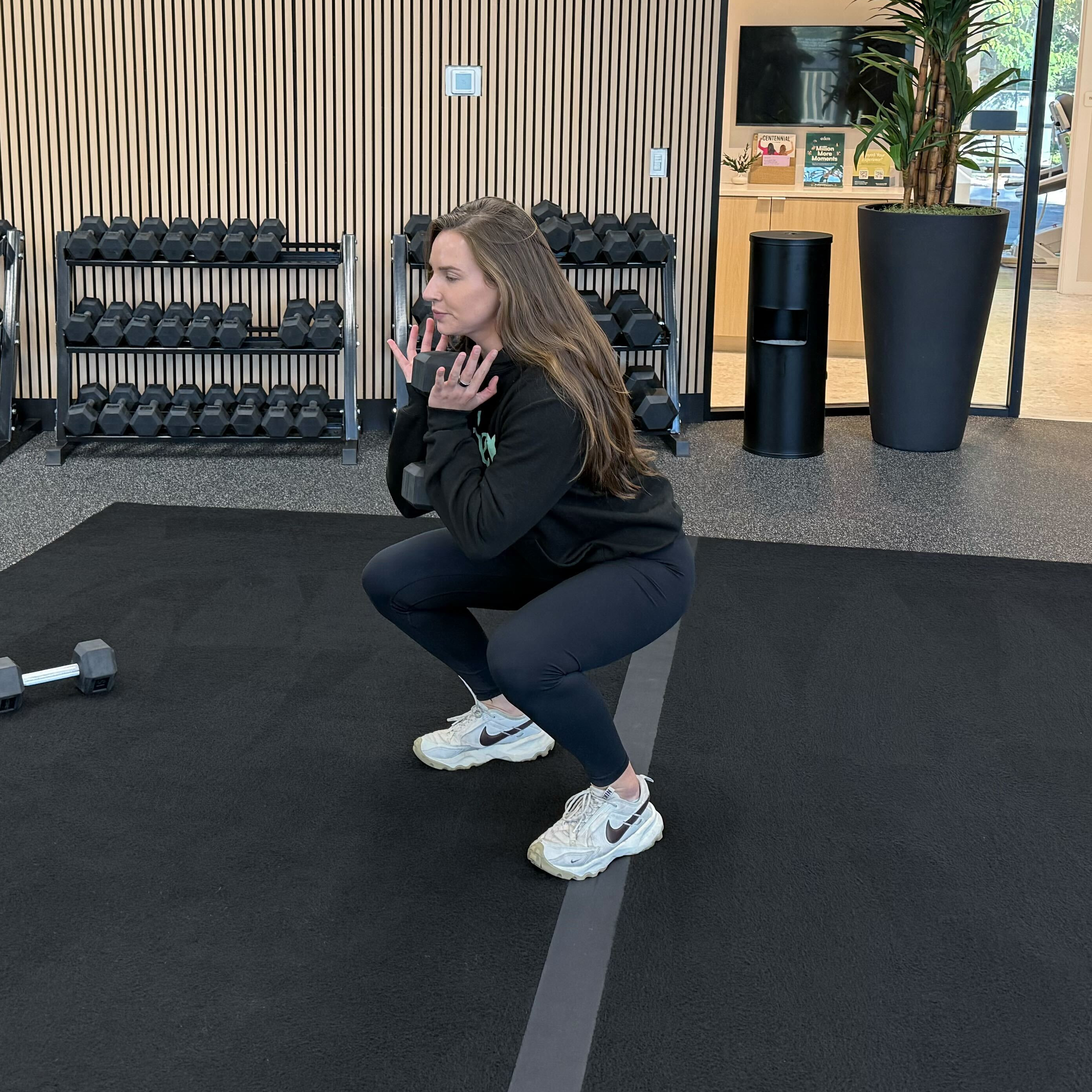 Felicia Hernandez, a personal trainer for Eden Health Club, performs a dumbbell goblet squat in a fitness studio. 