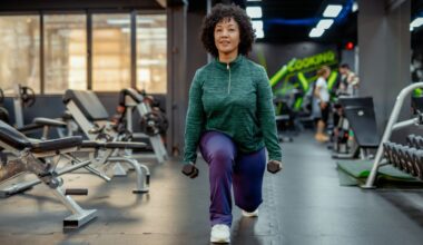 Woman doing reverse lunge, one of the best exercises for 60 and over in the gym holding dumbbells and wearing activewear