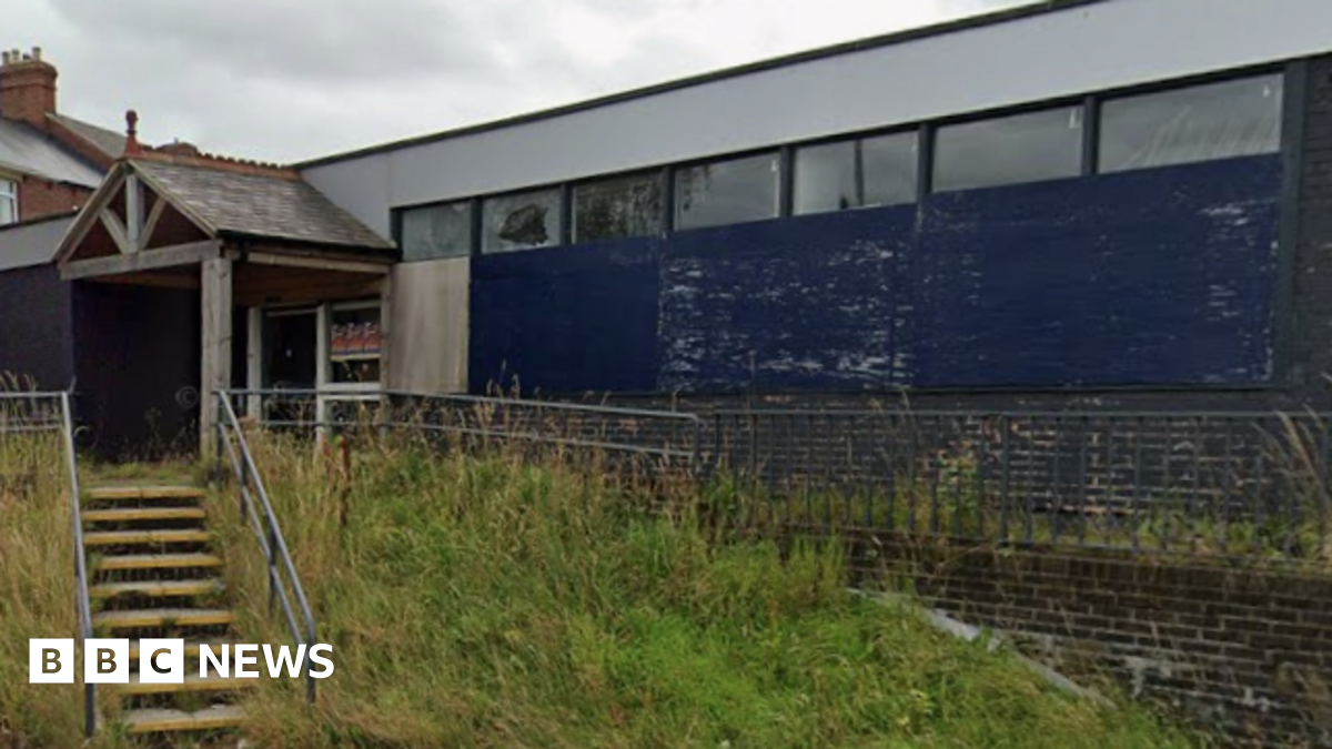 The former Stanley library is an empty one-storey building made of brown bricks and surrounded by overgrown grass.