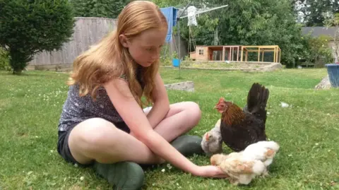 Family handout/PA Wire A picture of Ruth sitting on grass in what appears to be a back garden, with chickens eating food from her open hand.