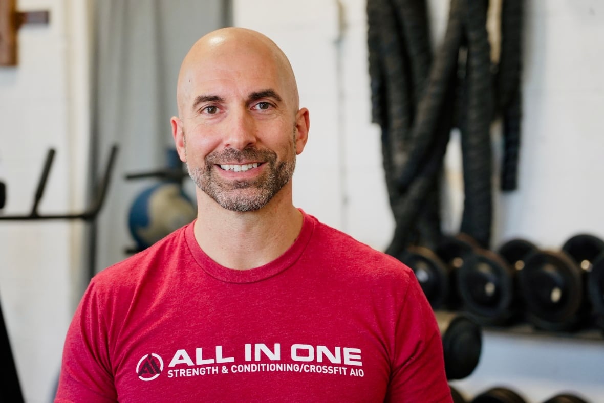 A man wearing a red shirt stands in a gym.