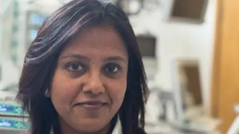 A smiling Dr Manjula Meda is pictured standing in front of an empty bed on Wexham Park Hospital's intensive care unit 