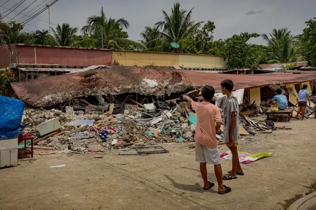 Residents look on next to a collapsed residential building on October 02, 2025 in Bogo, Cebu province, Philippines.
