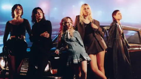 Cal Macintyre A promotional photo for The Last Dinner party shows the band leaning against a vintage car in a foggy urban landscape, illuminated by streetlamps
